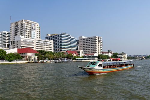 Free Vibrant riverboat cruising on the Chao Phraya River with modern Bangkok skyline in the background. Stock Photo