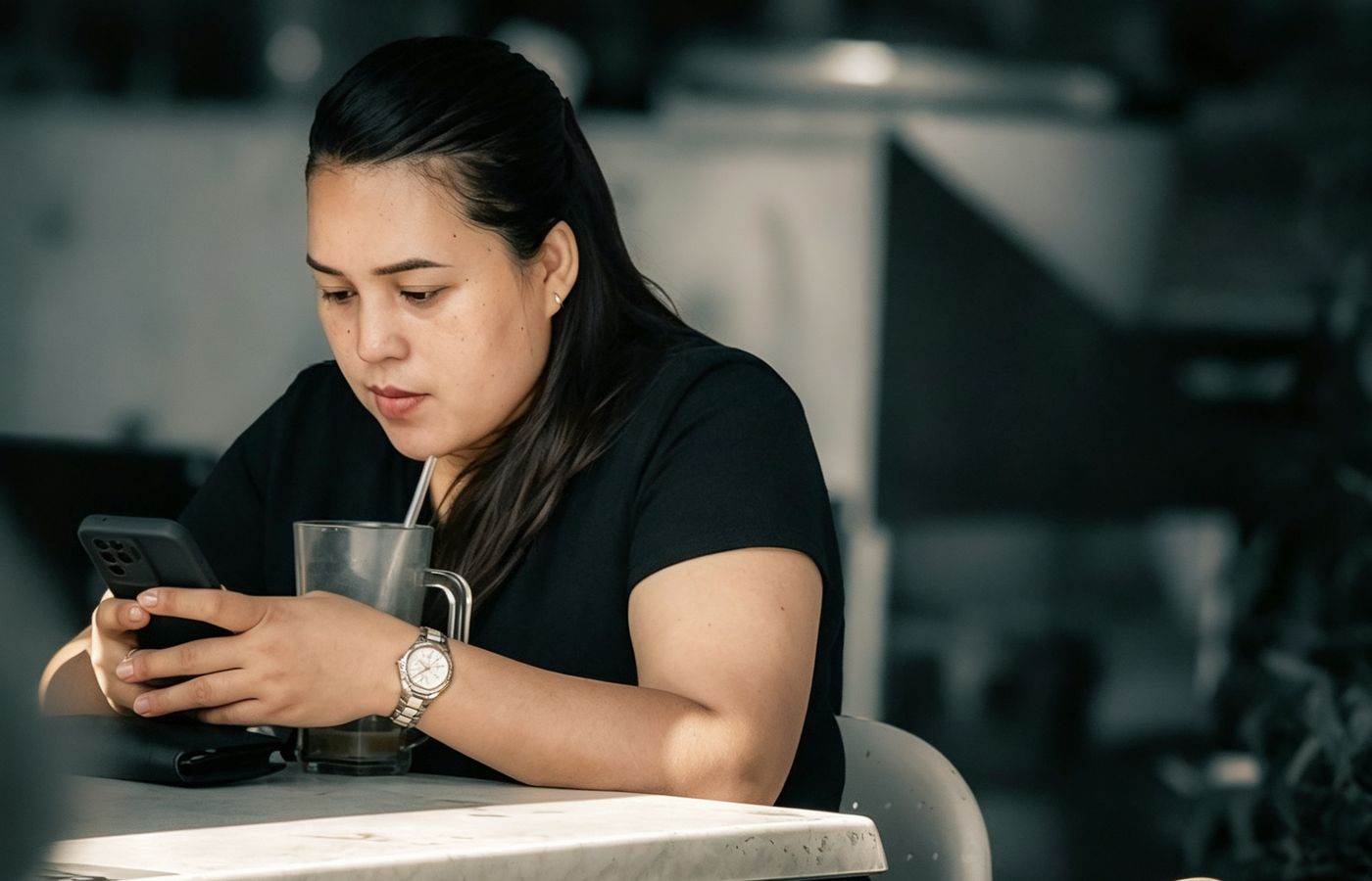 Woman sipping iced coffee while using smartphone at cafe. Relaxed indoor moment.