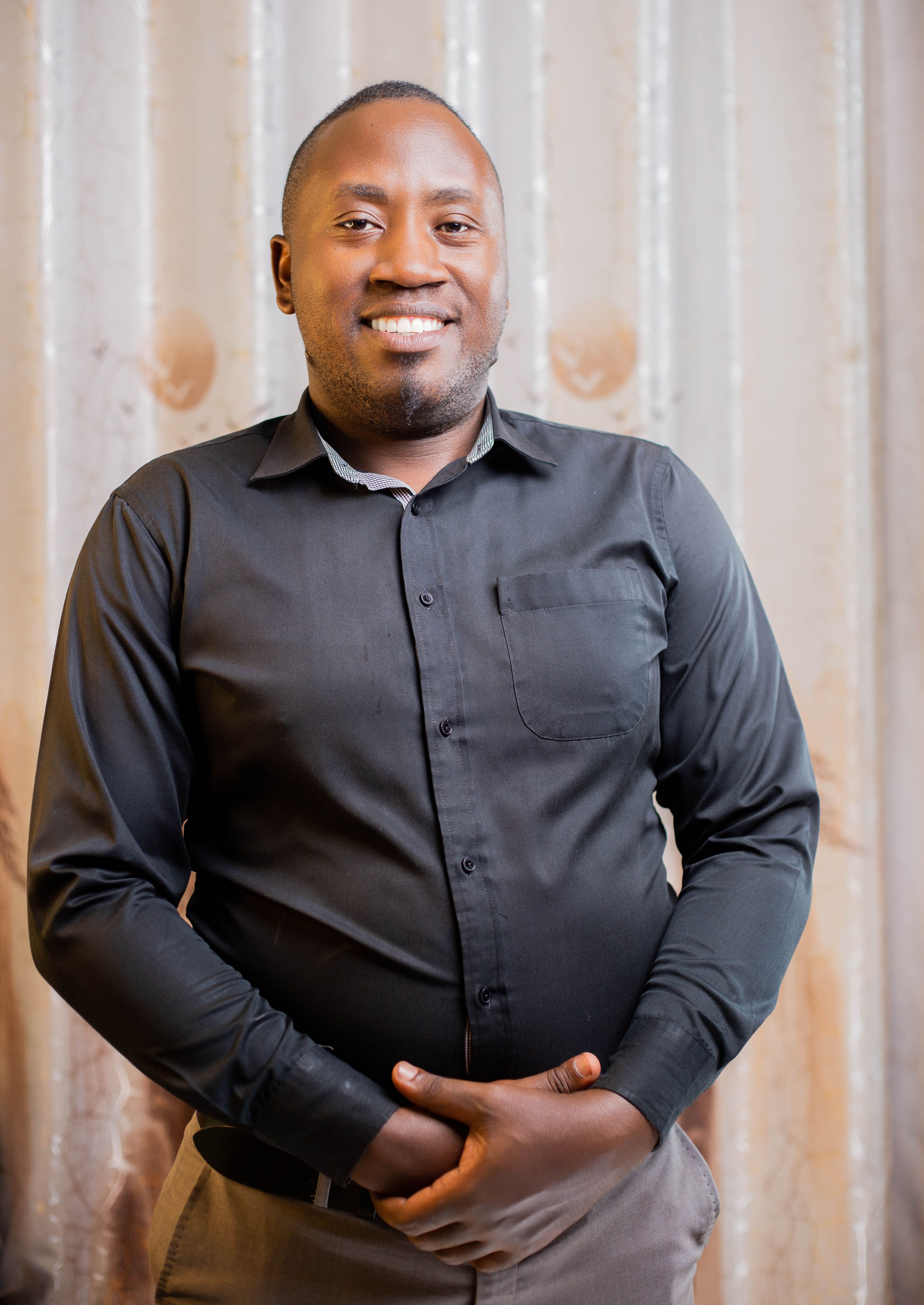 Portrait of a smiling man in a black shirt standing against a neutral background indoors.