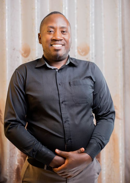Free Portrait of a smiling man in a black shirt standing against a neutral background indoors. Stock Photo