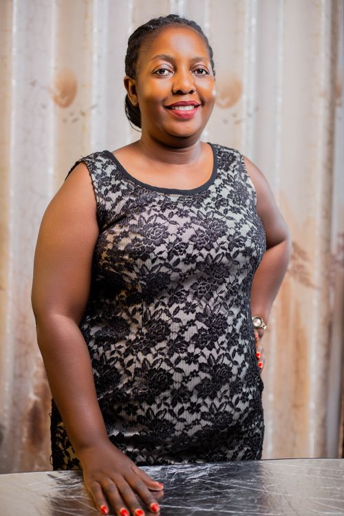 Free Portrait of a smiling woman in a black lace dress, standing indoors with a neutral backdrop. Stock Photo