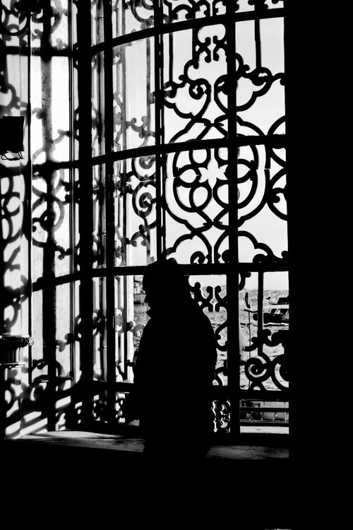 Free A person silhouetted against decorative window grilles creates a striking contrast in black and white. Stock Photo
