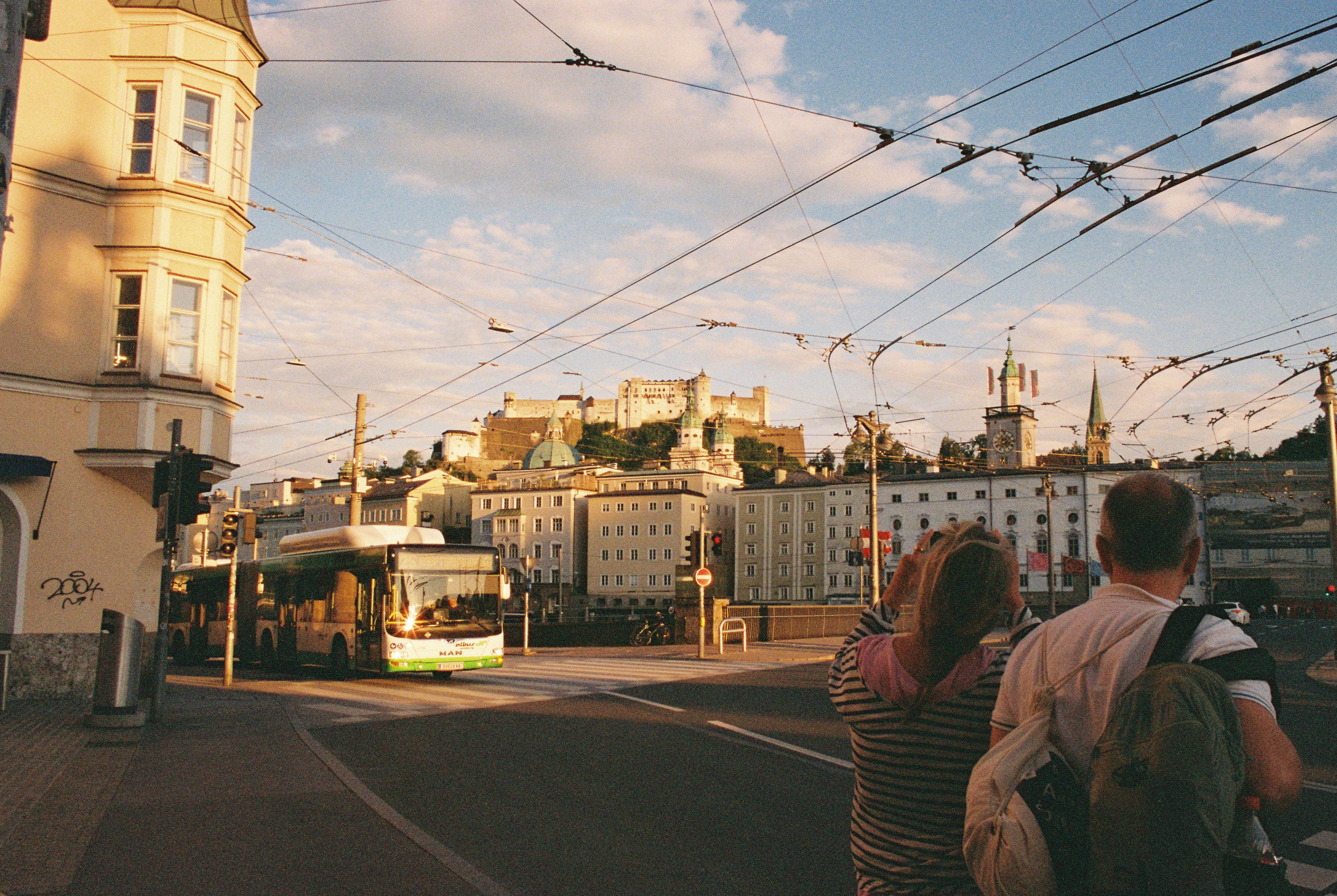 View of Salzburg from a bustling street corner, highlighting historic architecture and a passing bus at sunset.