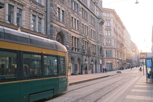 A scenic view of a tram on a historic street in Helsinki, Finland during sunrise.