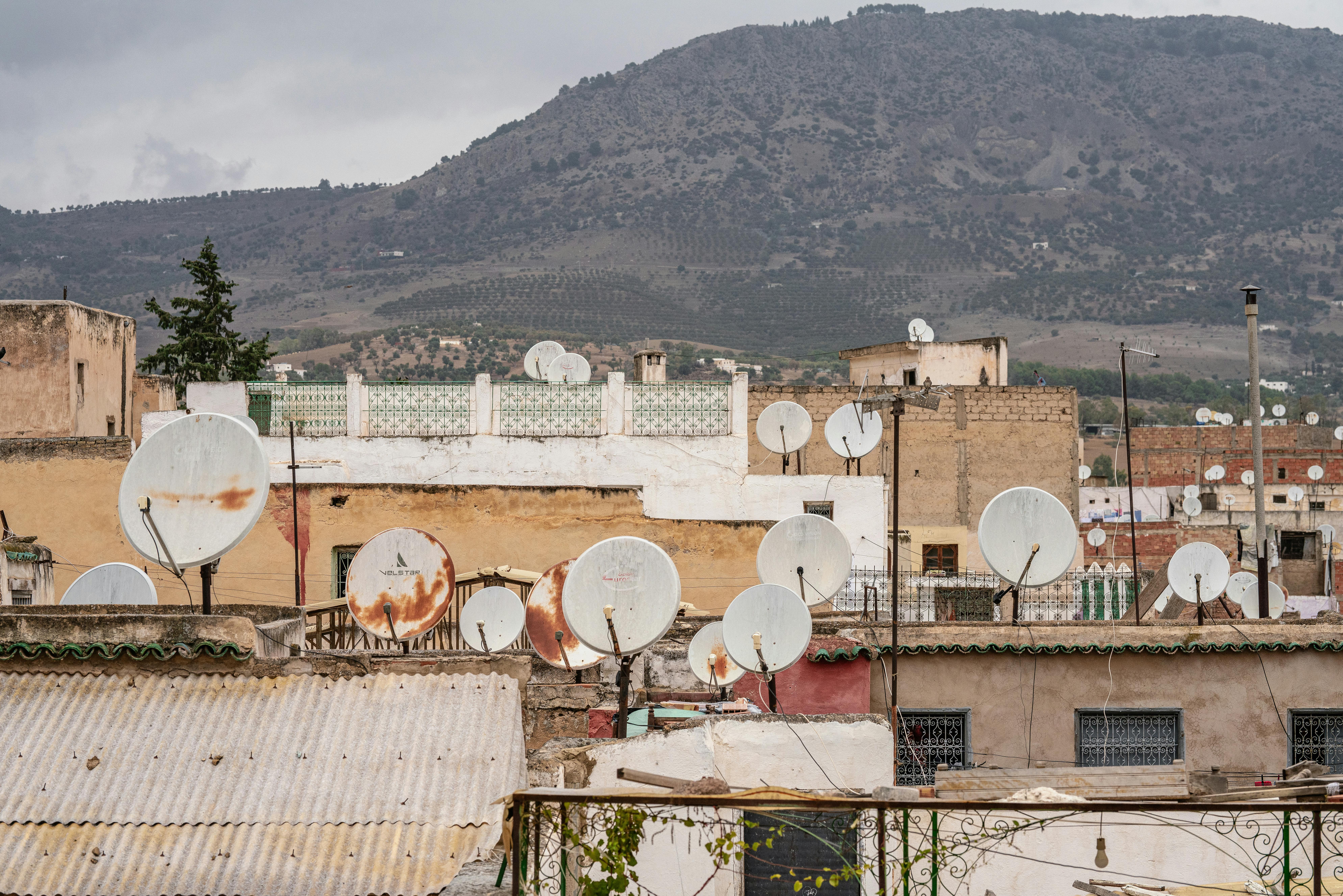 Rustic rooftops with satellite dishes in Fes, set against a rolling hill landscape.