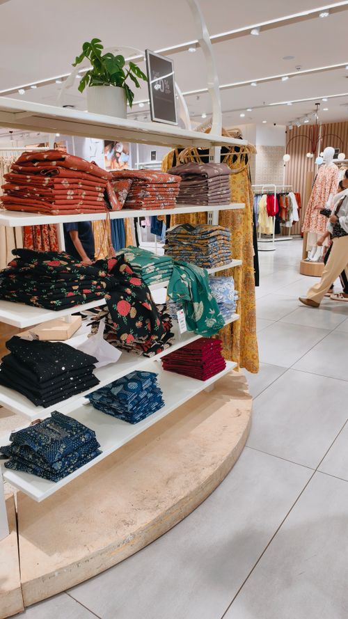 Free Retail store interior featuring colorful folded clothes on shelves and casual shoppers browsing. Stock Photo