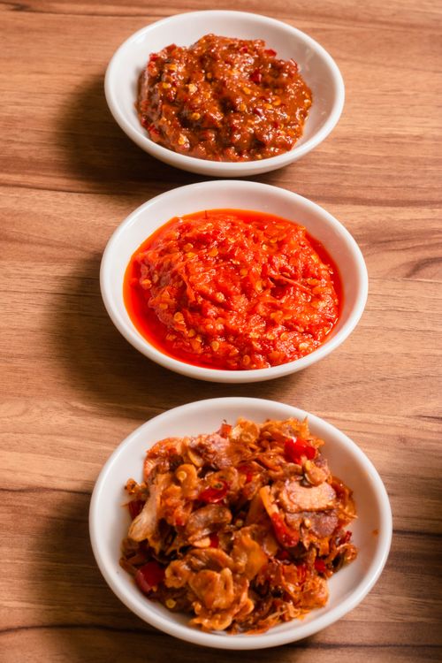 Free A variety of spicy chili sauces arranged in bowls on a wooden table, showcasing texture and vibrant colors. Stock Photo
