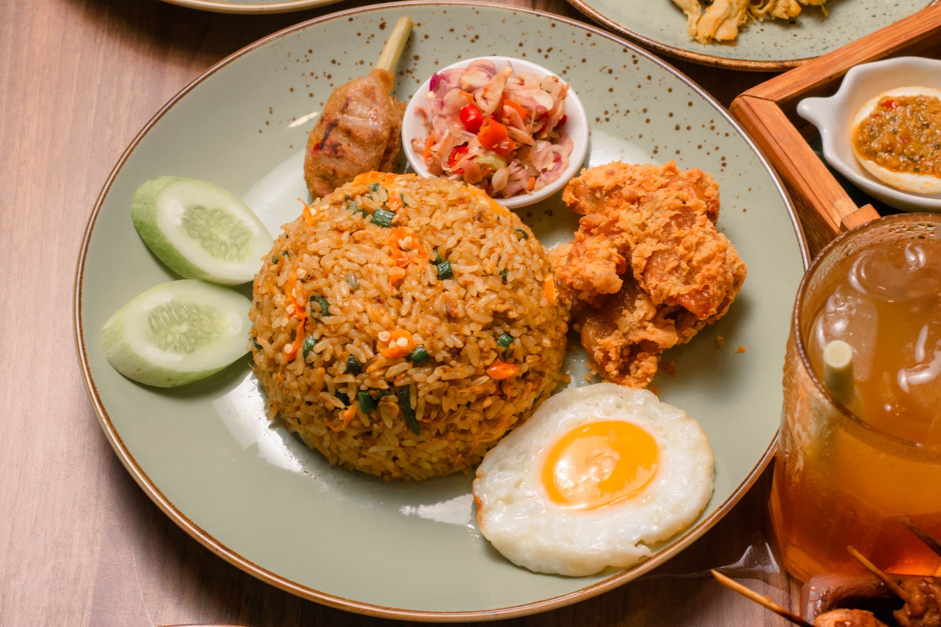 A plate of Nasi Goreng served with fried egg, satay, and iced tea. Perfect blend of flavors.