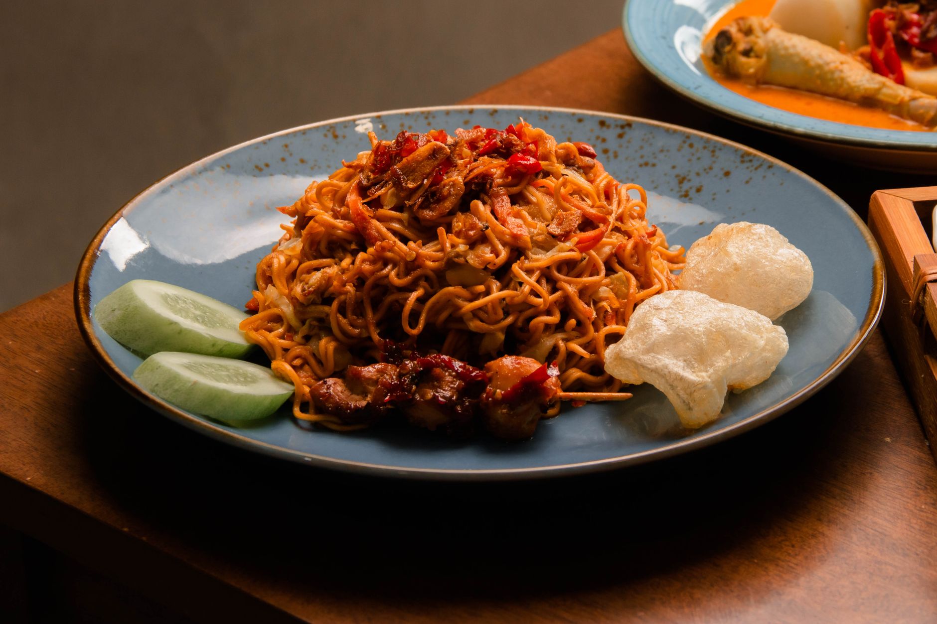 Plate of savory Asian noodles served with vegetables and crispy snacks.