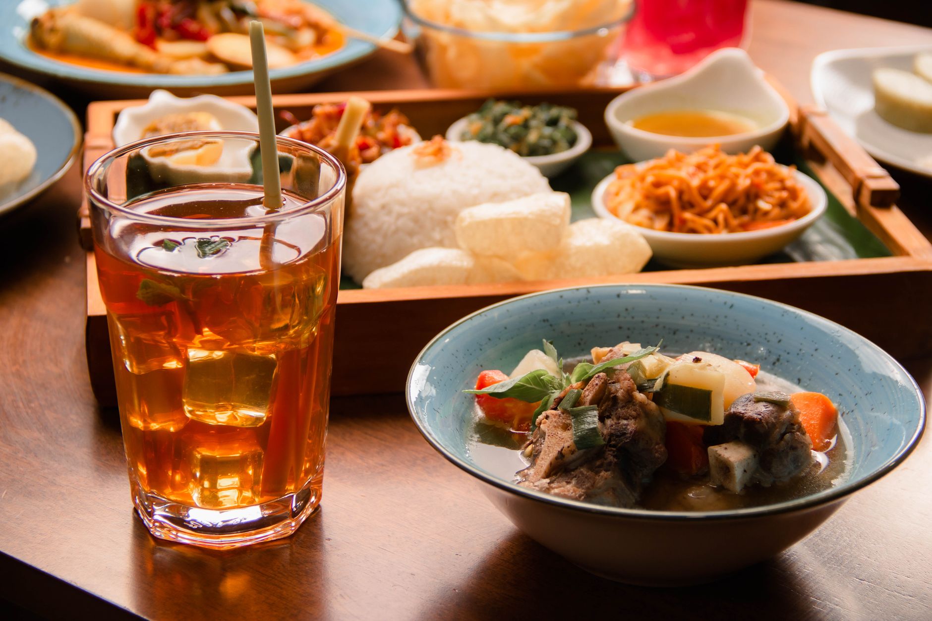 A vibrant spread of Indonesian dishes with a refreshing herbal drink served on a wooden table.