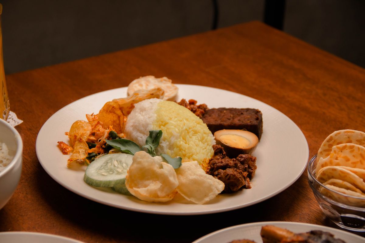 Nasi Padang platter with rice, egg, vegetables and beef rendang on a wooden table