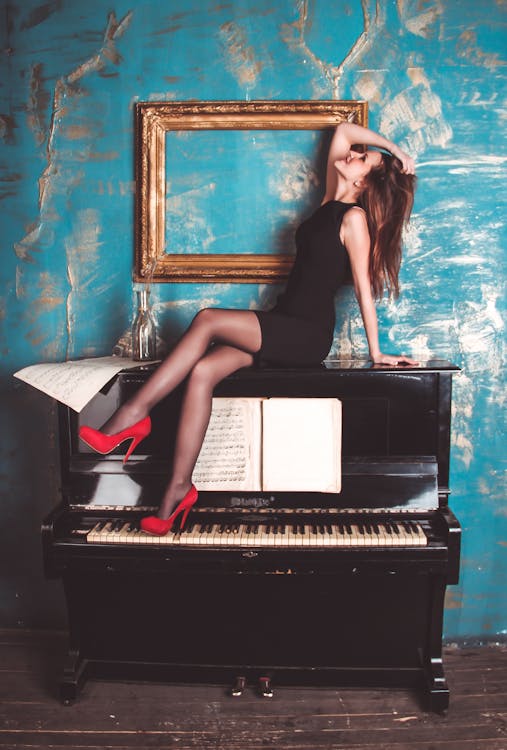 Gratis Seorang Wanita Duduk Di Piano Tegak Kayu Hitam Dekat Bingkai Foto Kayu Coklat Persegi Panjang Foto Stok