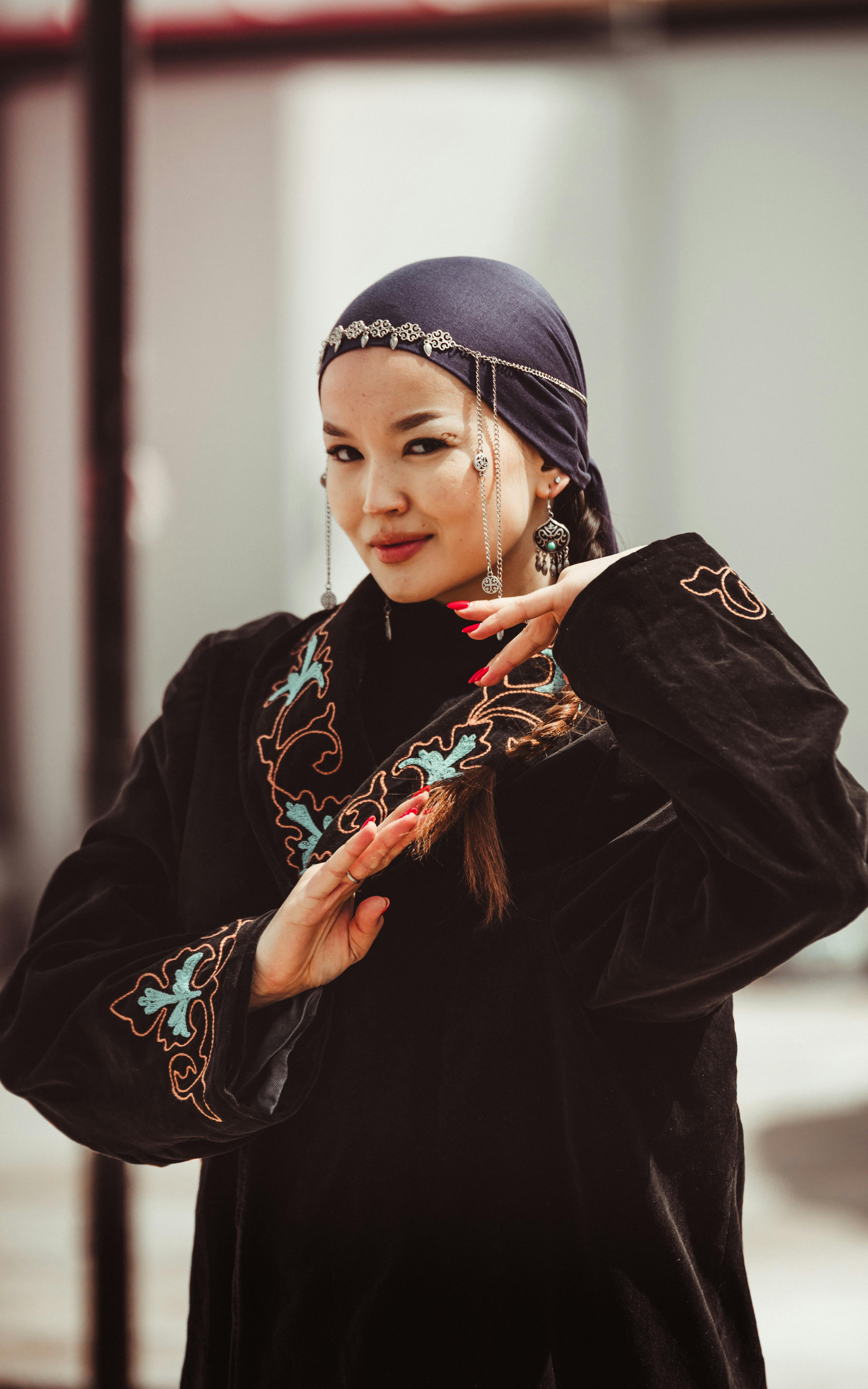 A woman in cultural dress poses gracefully with ornate embroidery, showcasing heritage.