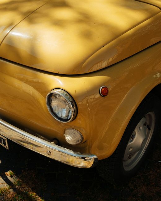 Detailed close-up of a classic yellow Fiat 500 car parked outdoors, showcasing vintage design.