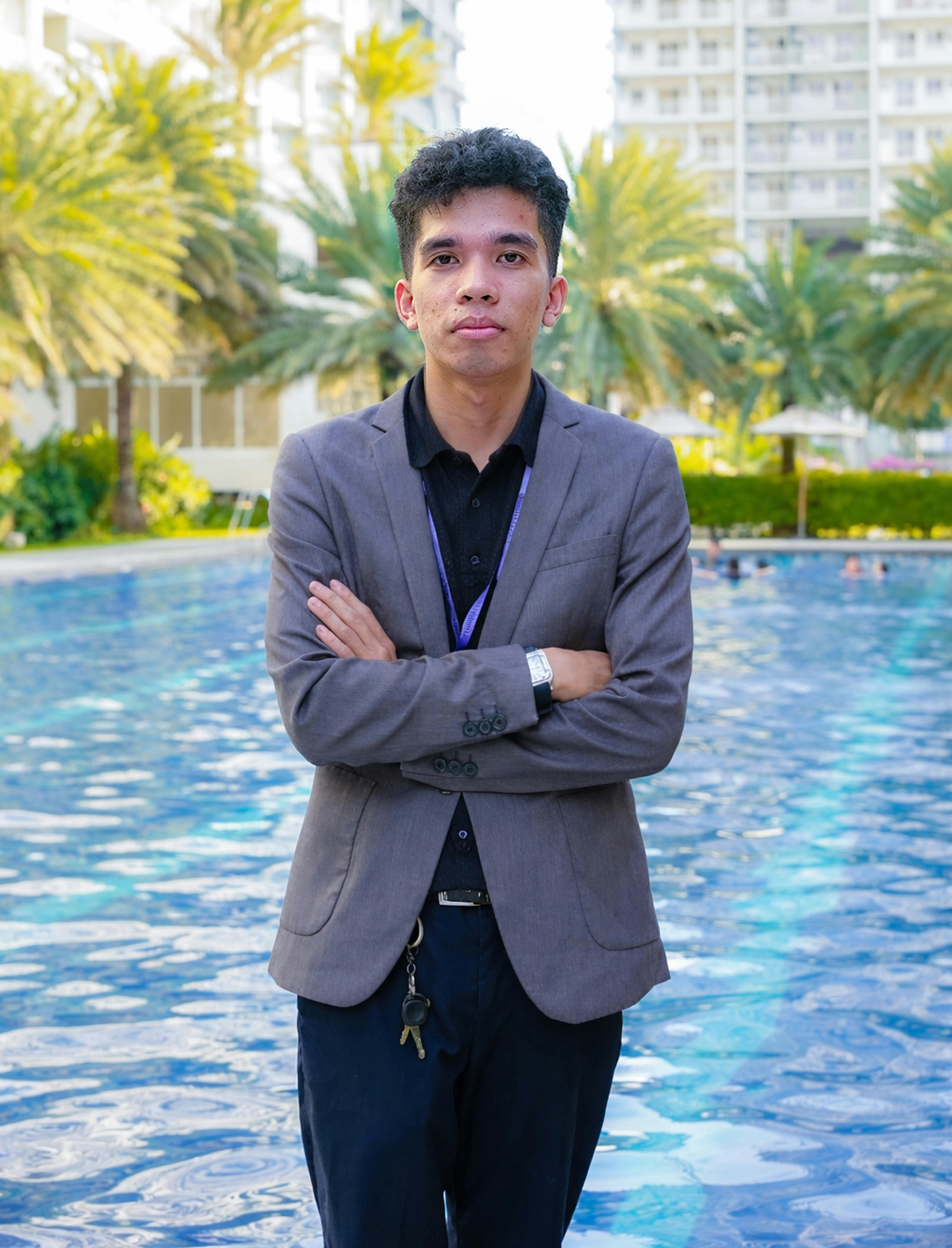 Young businessman in smart attire standing confidently by a poolside. Bright day setting.