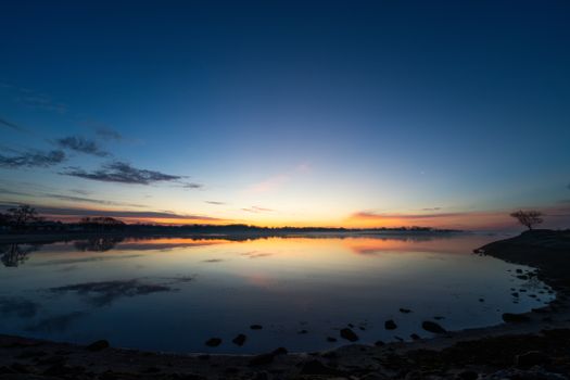 A peaceful sunrise with vibrant colors reflecting on a tranquil lake, creating a serene and soothing atmosphere.