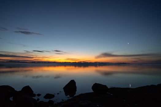 Peaceful sunset reflecting over calm ocean waters with rocks silhouetted against the colorful sky.