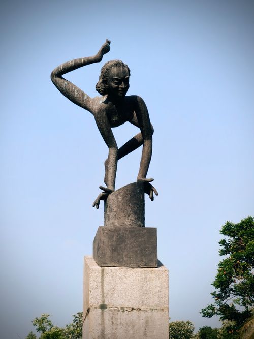 Free A striking sculpture of a traditional Indian dancer in a dynamic pose set against a clear blue sky. Stock Photo