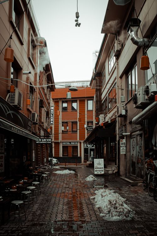 Free A narrow urban alleyway with restaurants and signs on a rainy day, showcasing a warm street vibe. Stock Photo
