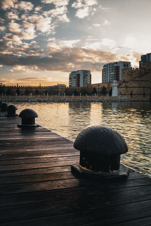 Free A picturesque waterfront view at sunset with modern buildings and a boardwalk. Stock Photo