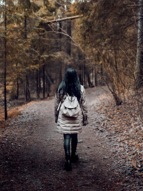 Woman Carrying a Backpack  Walking on Pathway Surrounded by Trees