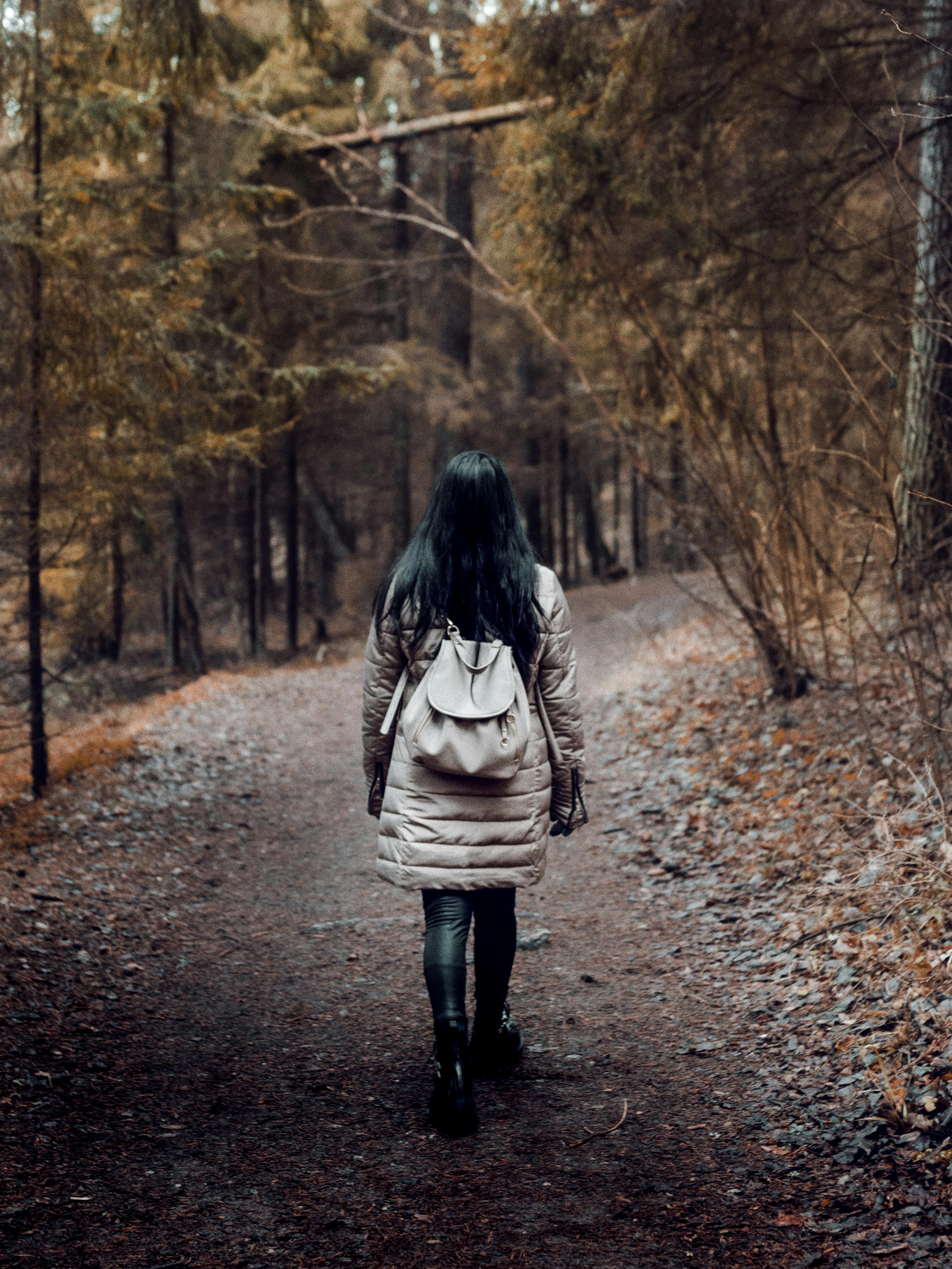 Woman Carrying A Backpack Walking On Pathway Surrounded By Trees