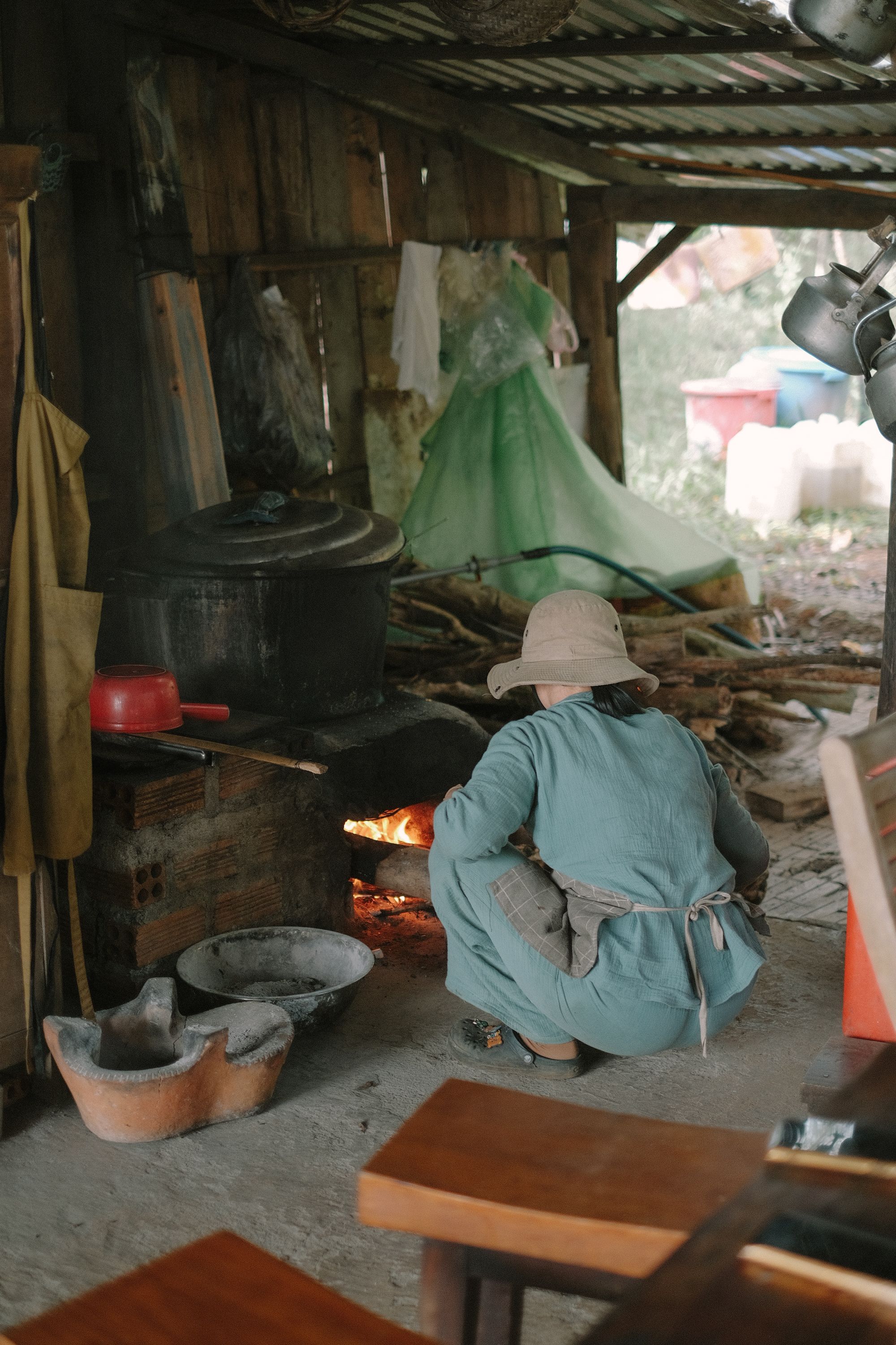 Person cooking at a traditional outdoor wood stove, rustic setting.