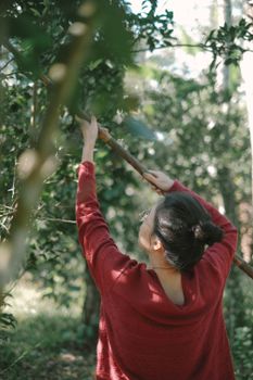 A woman in red reaches to pick fruit from a tree in a verdant outdoor setting.