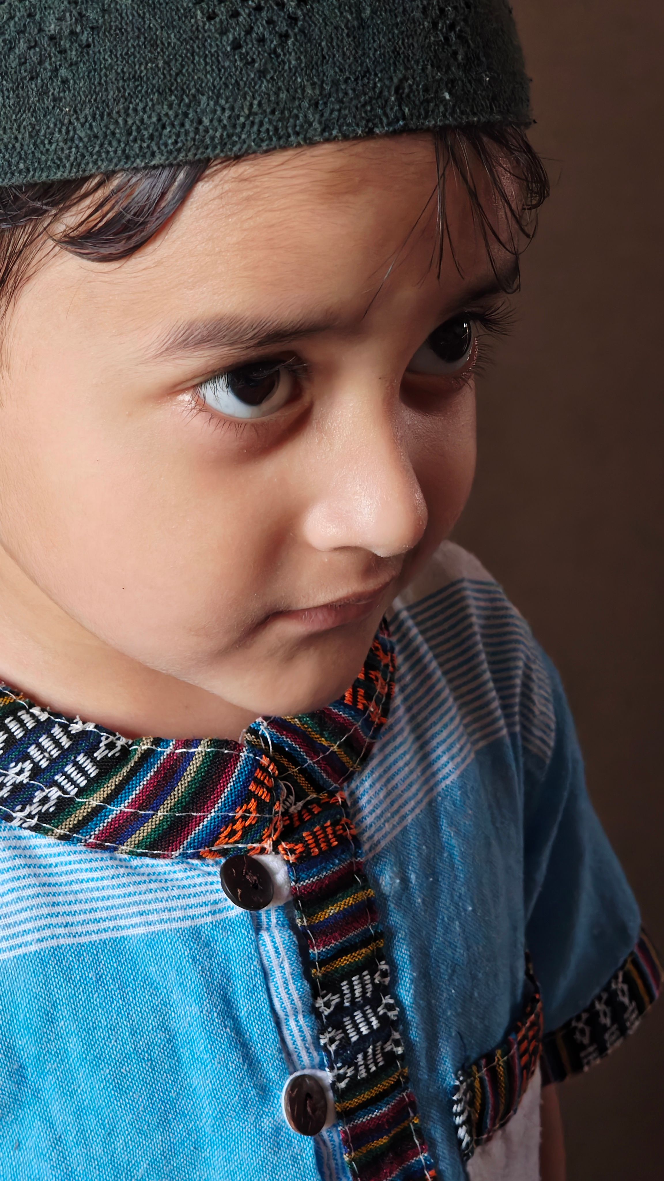 Close-up portrait of a young boy wearing a cap and patterned shirt, expressing contemplation.