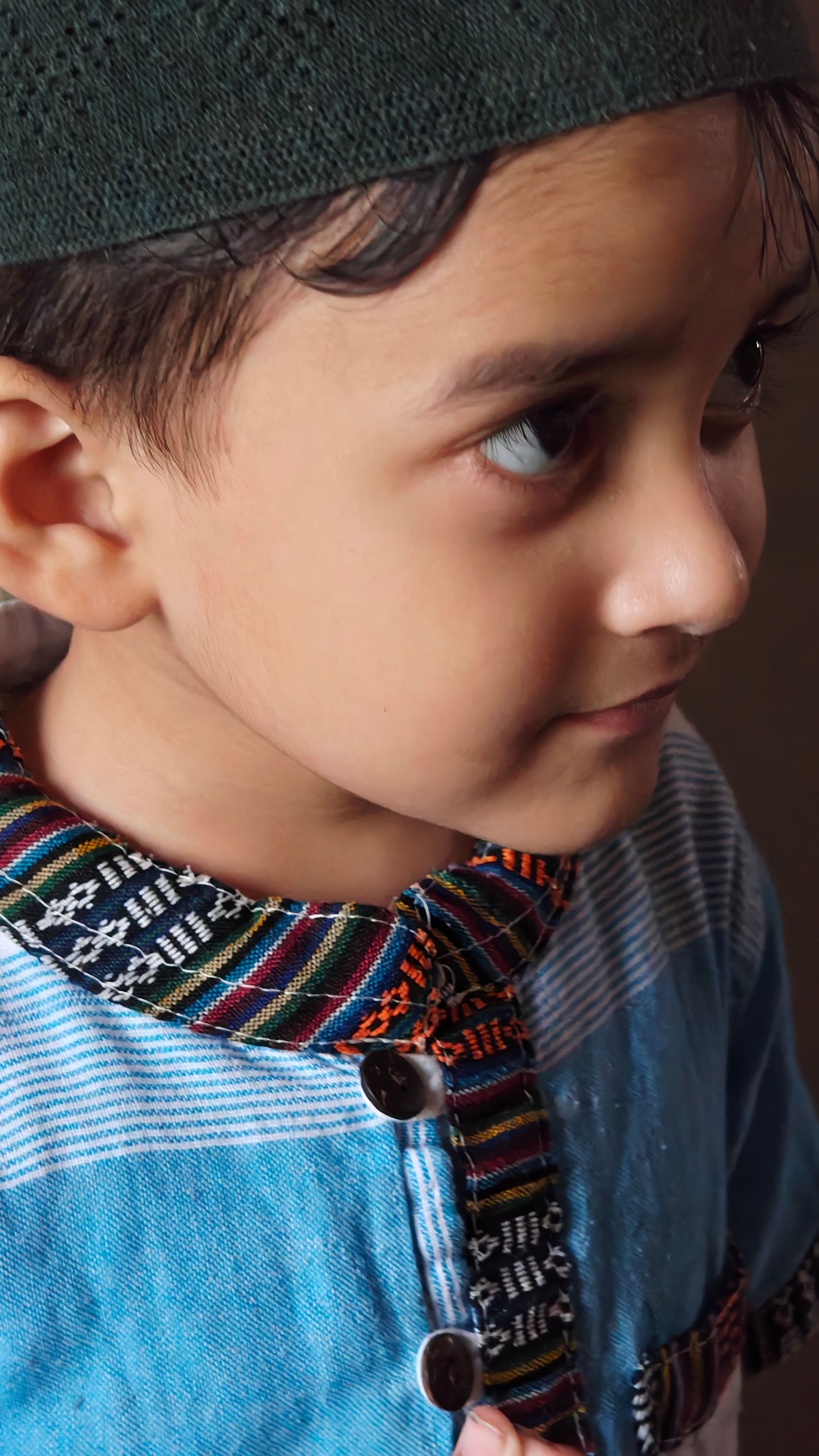 Close-up portrait of a young child wearing a colorful traditional outfit, looking thoughtful.