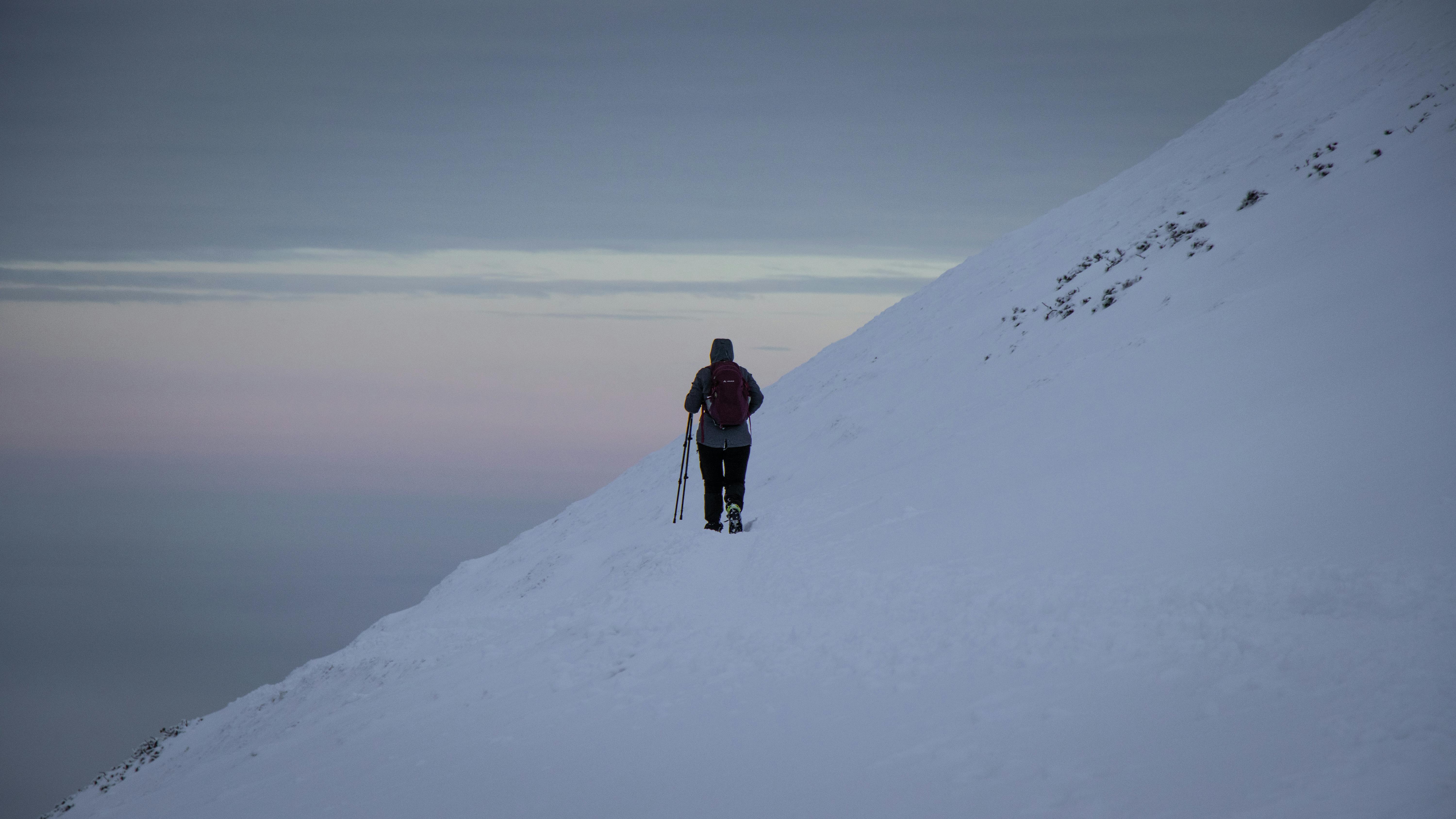 A lone hiker traverses a snowy mountain slope at twilight, capturing the serene winter landscape.
