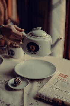 A serene morning scene featuring a white teapot, empty plate, and newspaper on a table.