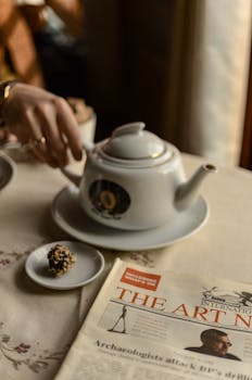 A cozy morning scene with a teapot, newspaper, and snack on a table, evoking relaxation.
