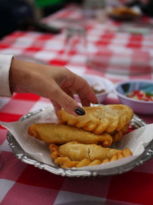 Free A hand reaches for delicious empanadas on a picnic table with a red checkered cloth. Stock Photo