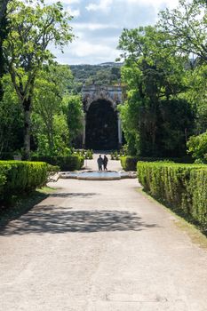 A serene garden path with lush greenery leading to a historic archway in a peaceful setting.