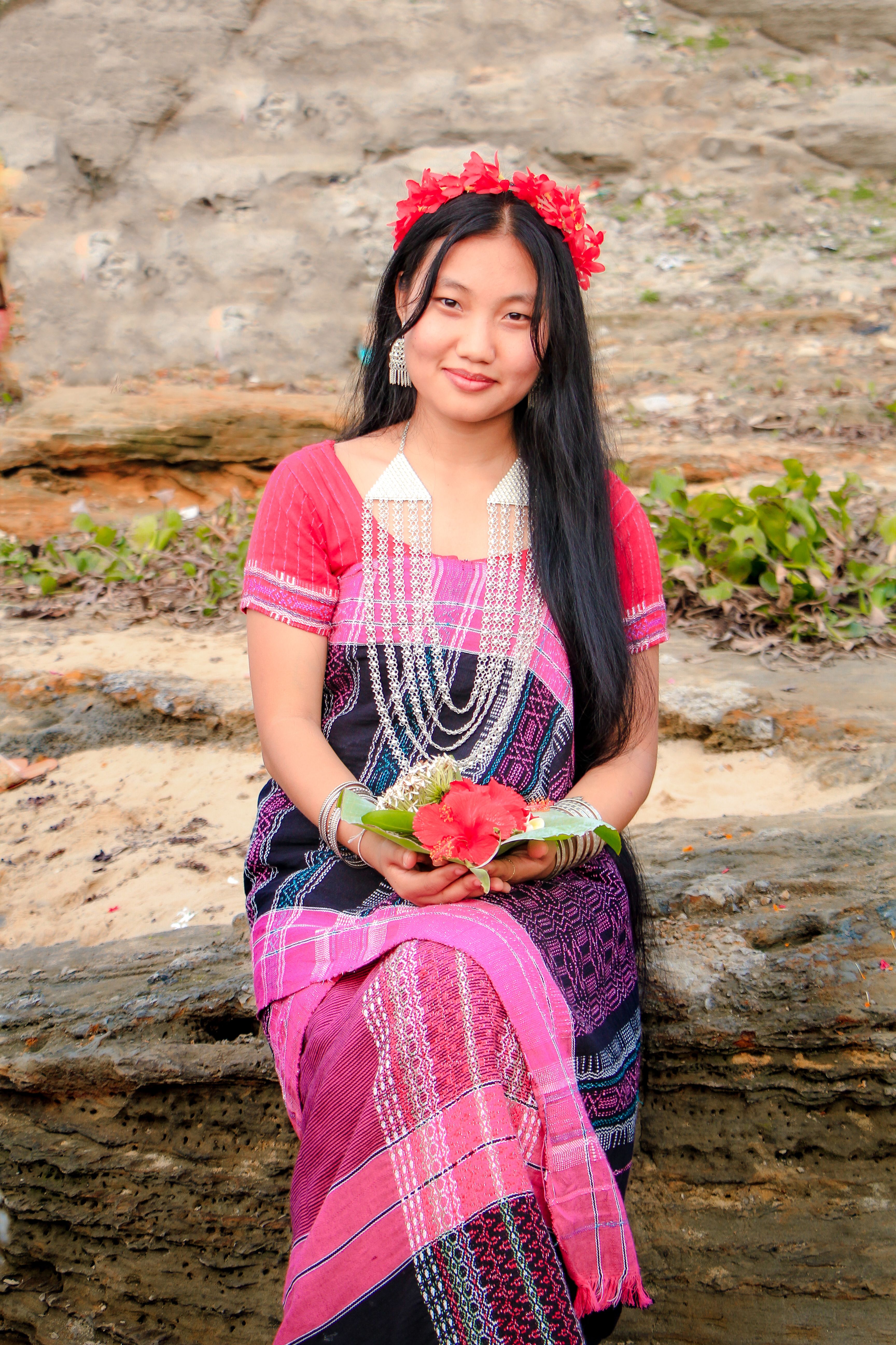 A Chakma woman in Rangamati wearing colorful attire and holding flowers, symbolizing cultural heritage.