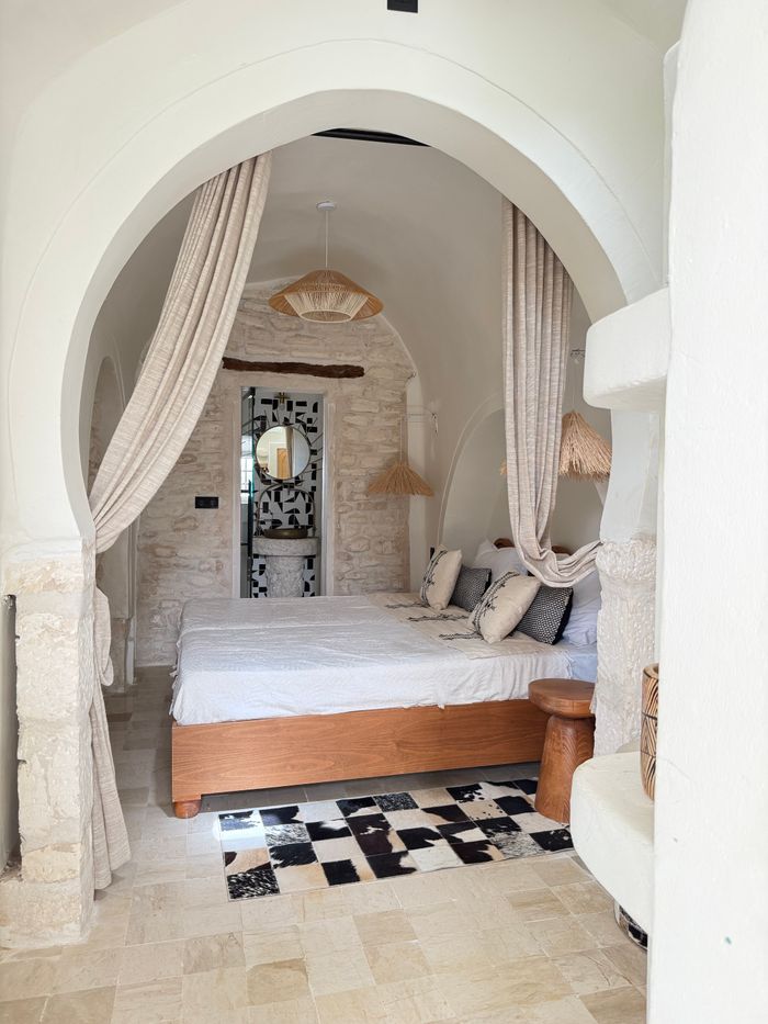 A limestone arch hung with linen curtains opening onto a bedroom with a stone floor