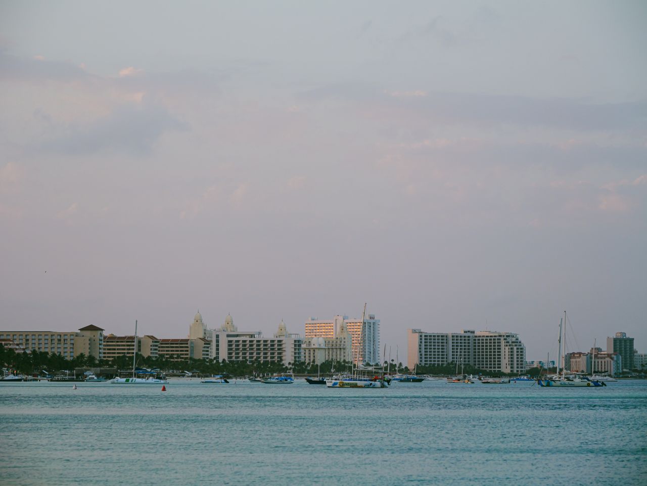 A serene view of a coastal cityscape with boats and buildings at twilight, under a pastel sky.