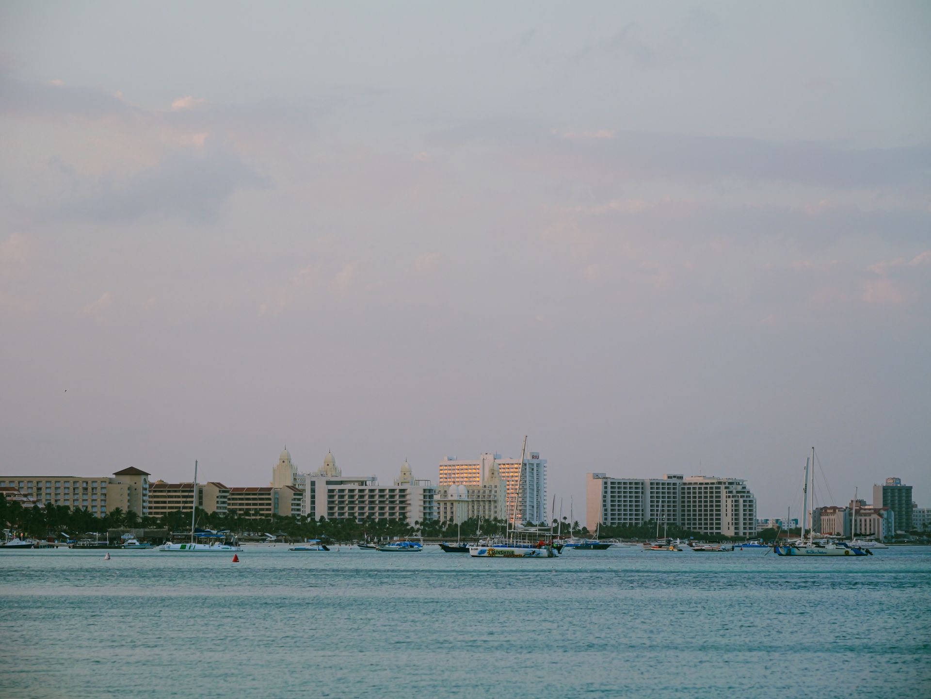 A serene view of a coastal cityscape with boats and buildings at twilight, under a pastel sky.