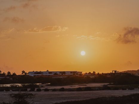 A vibrant sunset casting a warm glow over a coastal landscape with silhouetted buildings.