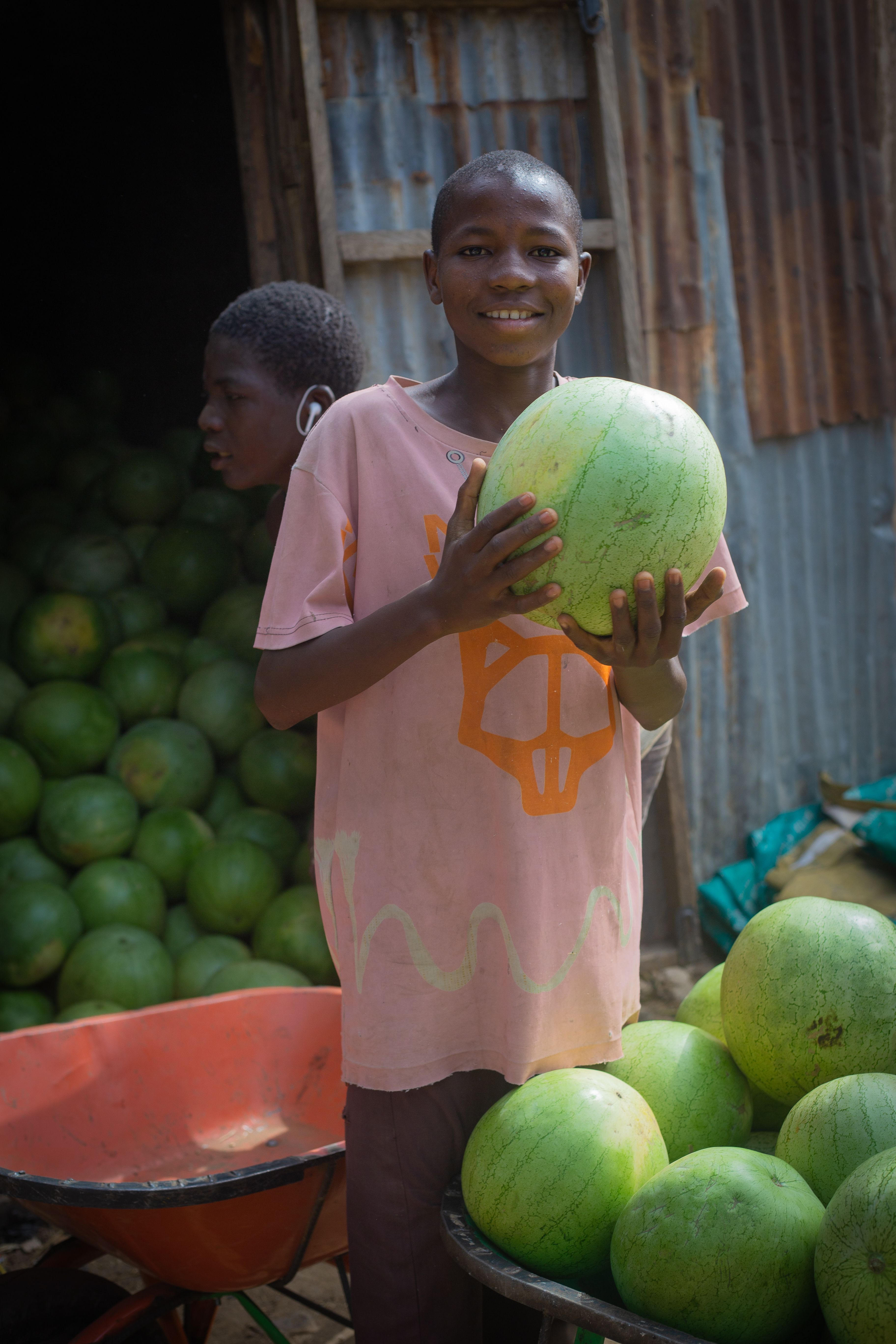 Un jeune vendeur souriant tient une pastèque devant son étal de fruits