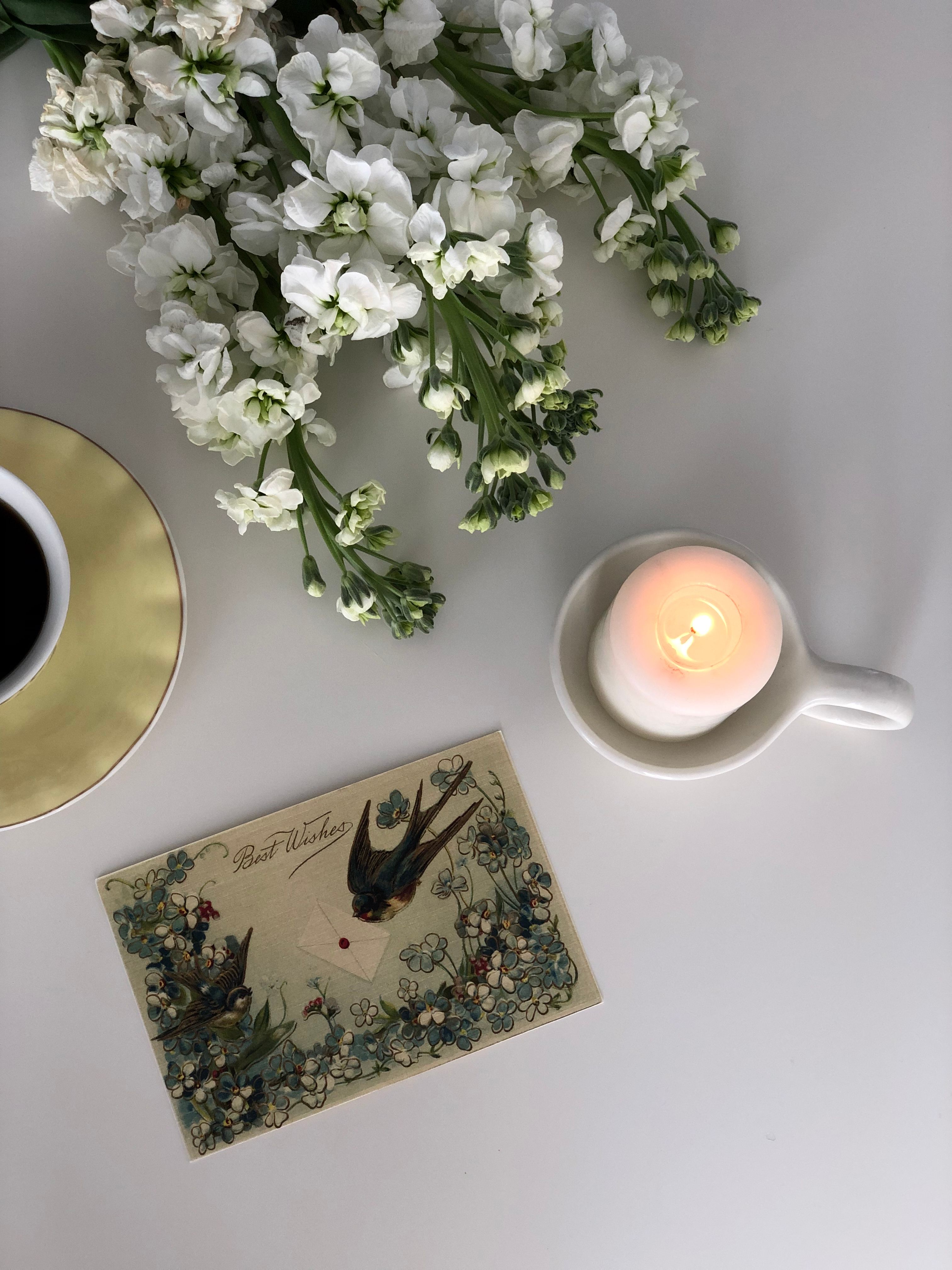 A serene composition of white flowers, lit candle, and vintage card on a table.