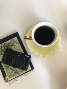 Cup of black coffee beside a compact Sony camera on white table.