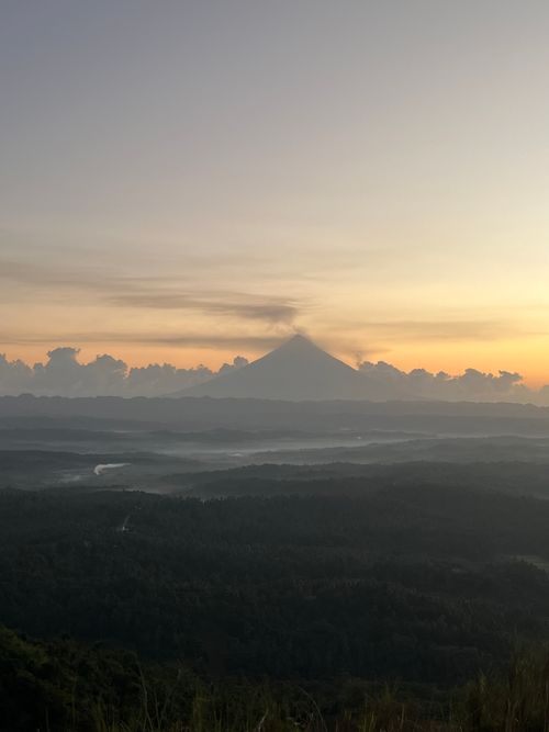 Free A breathtaking view of a volcano silhouette at sunrise, casting shadows over a lush landscape. Stock Photo