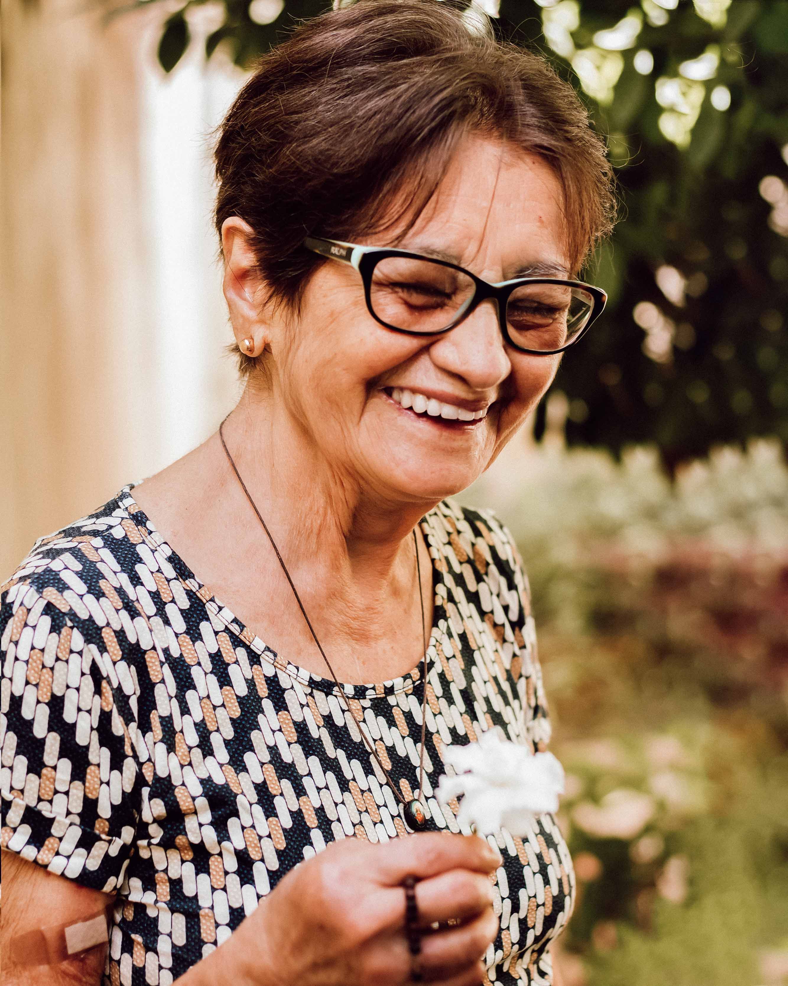 Senior woman with glasses, smiling joyfully outdoors while holding a flower, exuding happiness