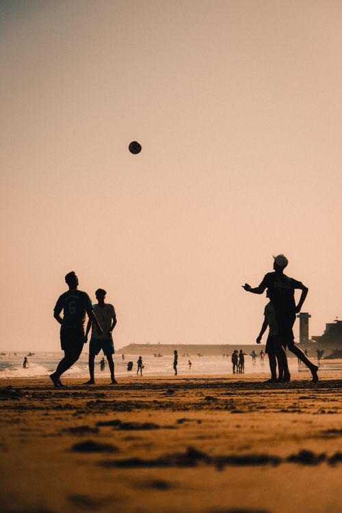 Free Dynamic silhouettes of people playing soccer on a beach during a stunning sunset, creating a relaxed and vibrant atmosphere. Stock Photo