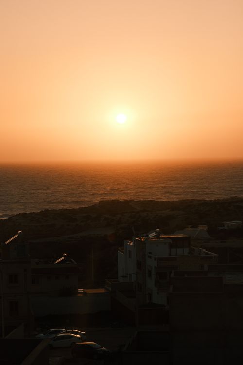 Free Beautiful sunset over ocean horizon with silhouetted coastal buildings below. Stock Photo