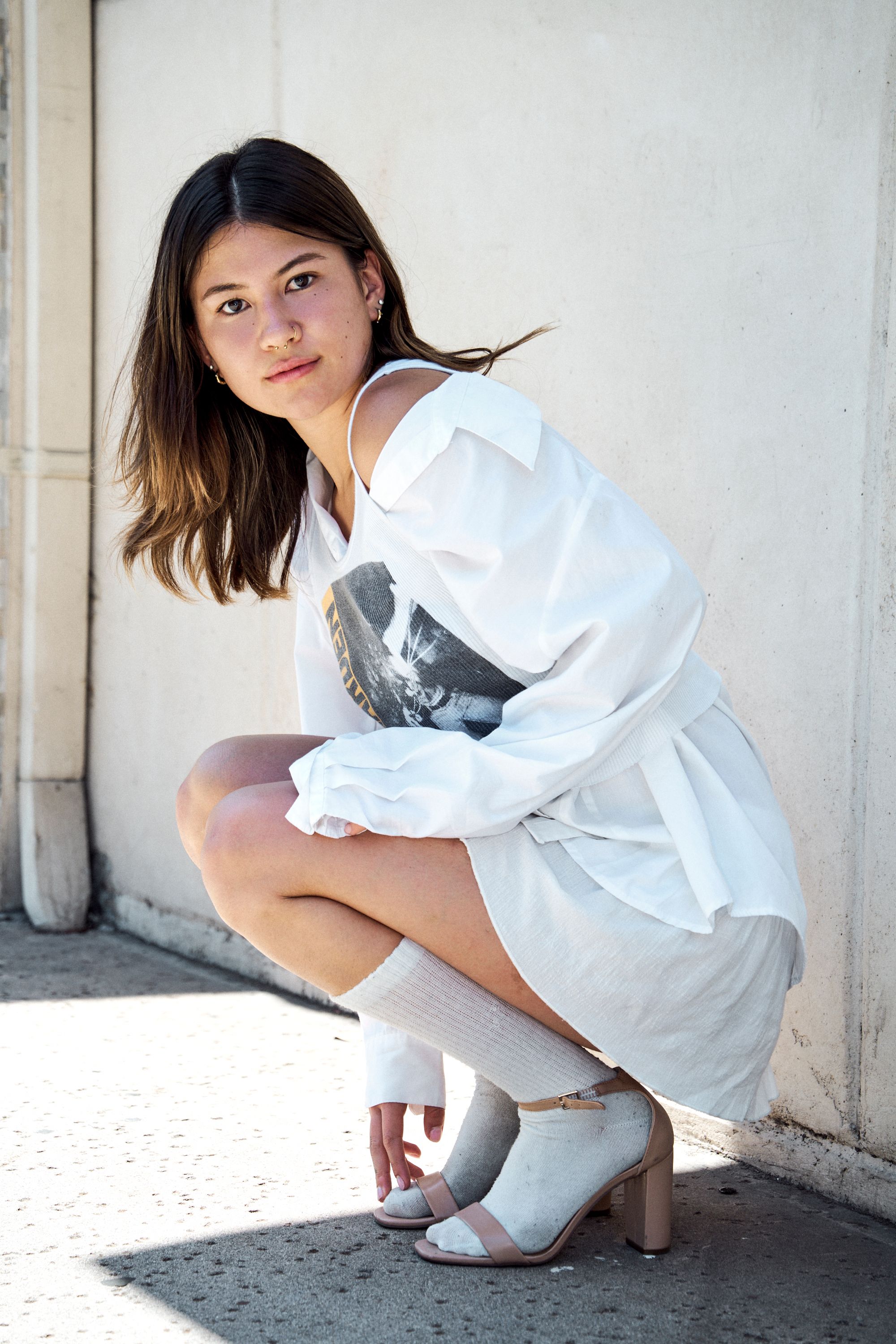 Stylish young woman in white outfit posing against a wall, showcasing modern fashion.