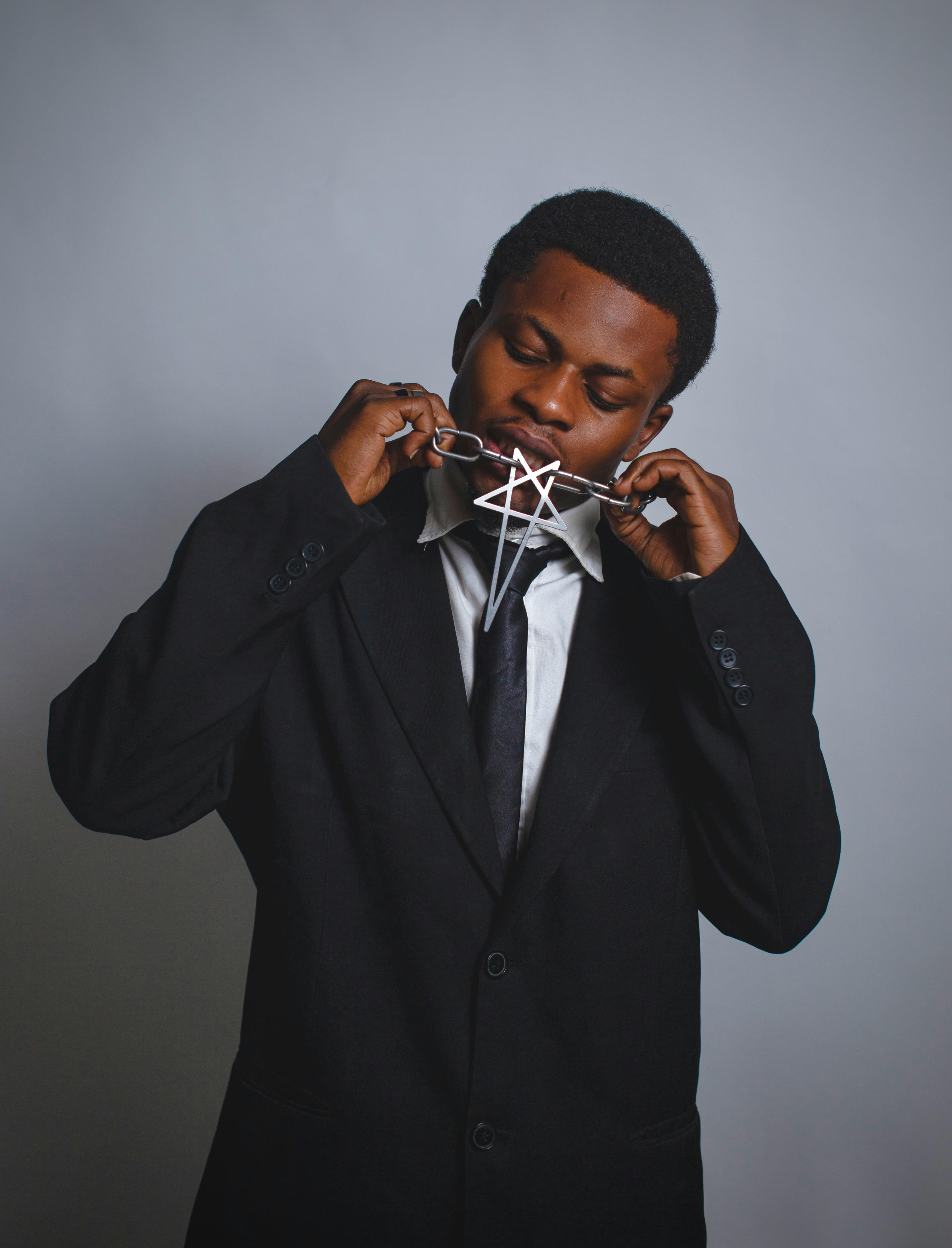 A man in a suit holding a star-shaped necklace against a neutral background.