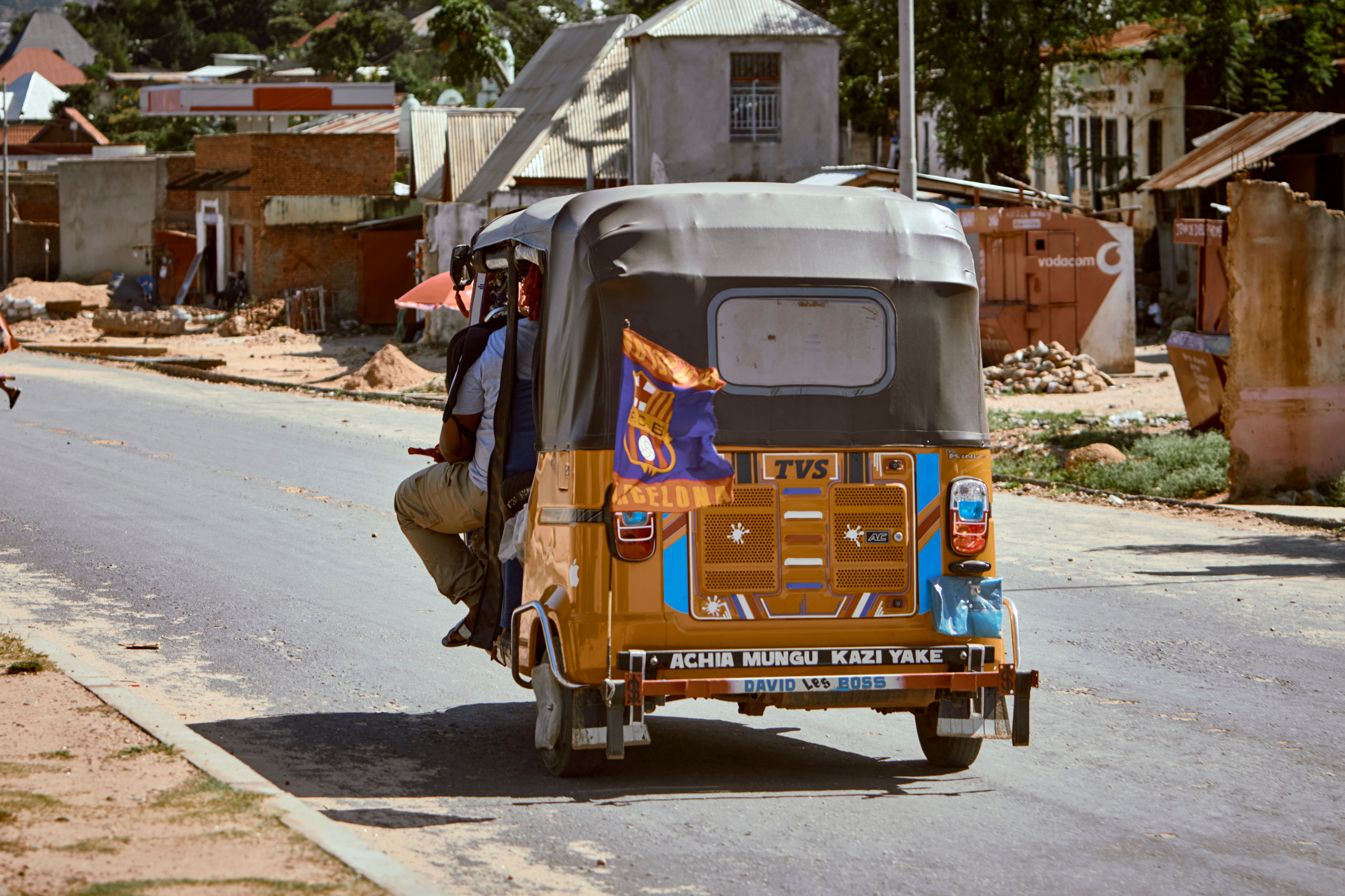 A bright tuk-tuk navigates a bustling urban road in a sunny locale.
